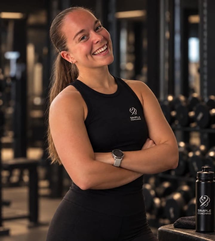 Coach Maria i Simple Coaching-klær, smilende med armene i kors i et treningsstudio